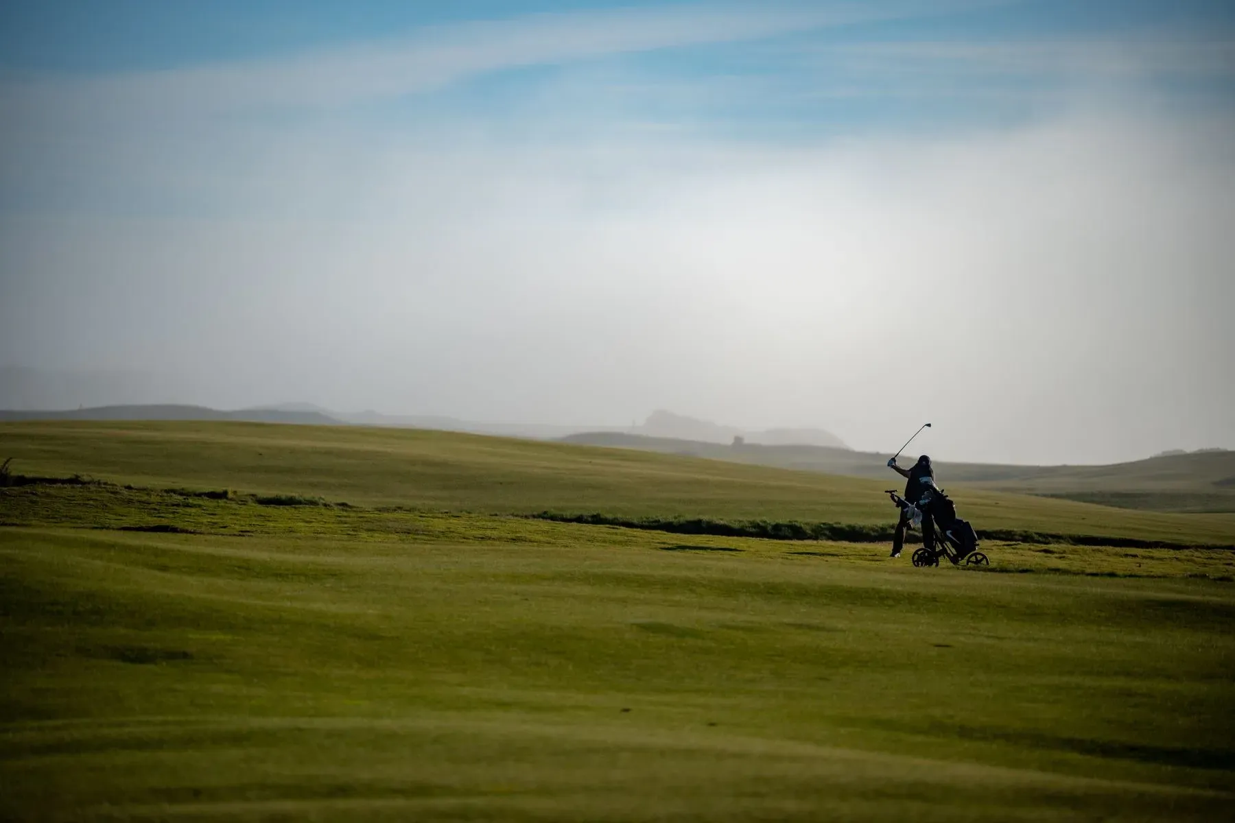 A golfer crossing an open links course in changing weather