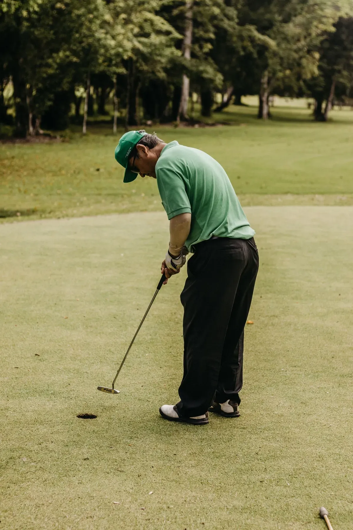 A golfer reading a putt on a tree-lined green