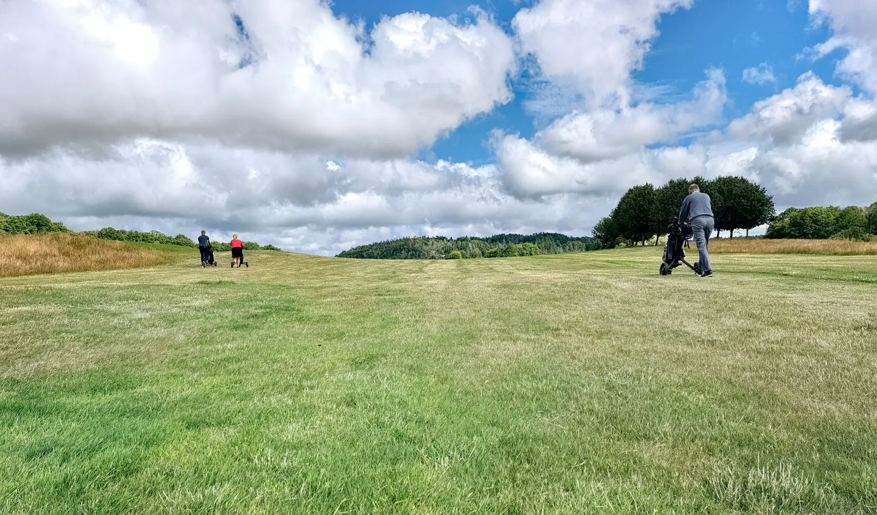 Golfers walking a wide fairway under an open sky
